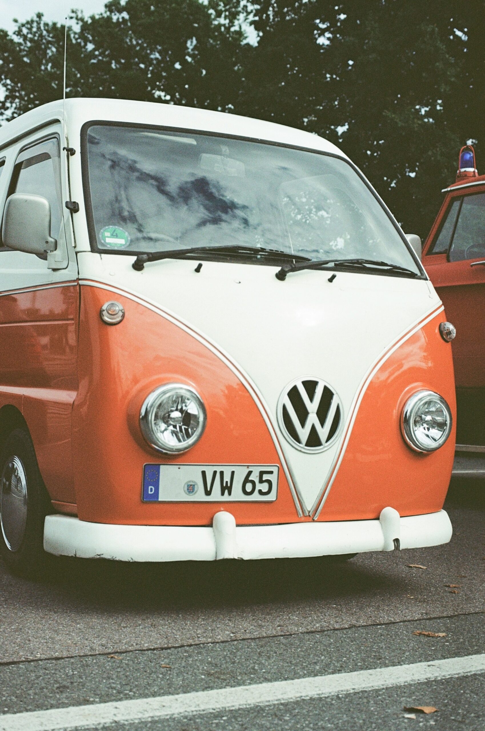 an orange and white vw bus parked next to a red car